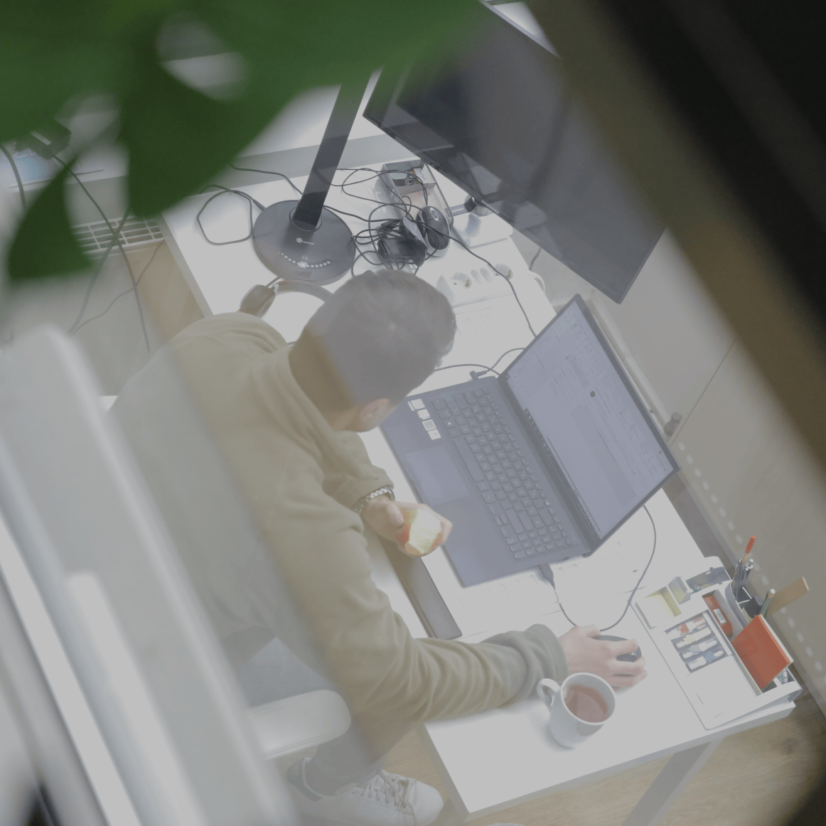 Person arbeitet an einem Laptop am Schreibtisch im Büro, aufgenommen aus erhöhter Perspektive
