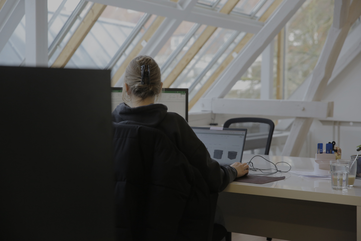 Person arbeitet an einem Laptop im Büro mit schrägen Dachfenstern im Hintergrund