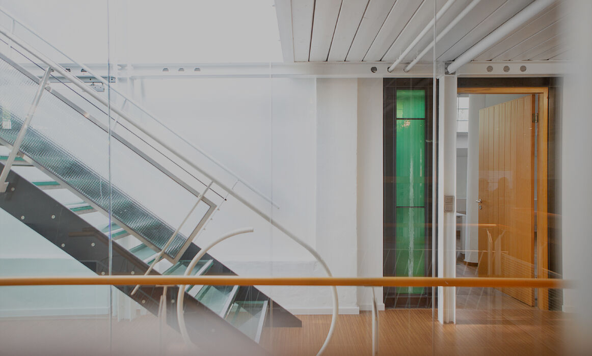 Heller Büroflur mit moderner Glas- und Metalltreppe und offenem Raum mit grünem Glaselement