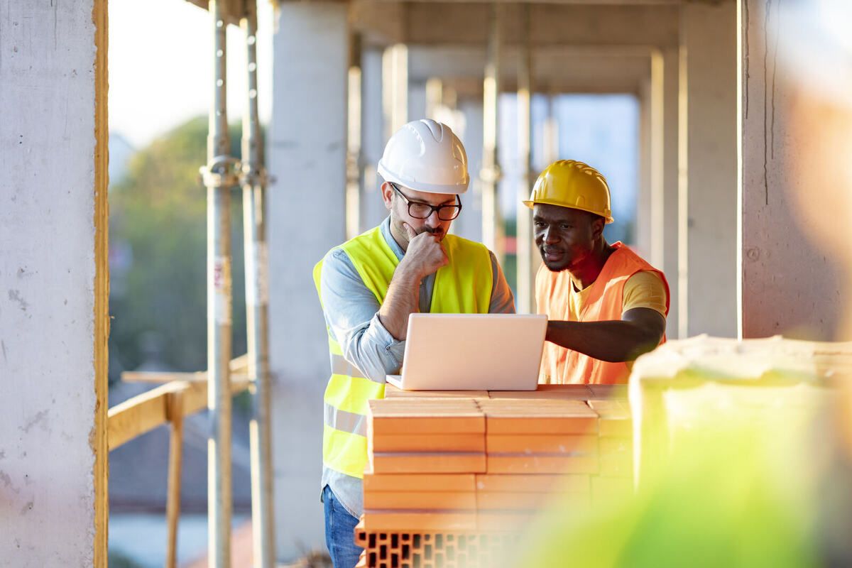 Zwei Bauarbeiter arbeiten mit dem Laptop auf der Baustelle