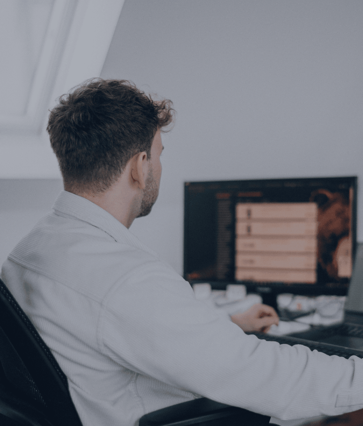 Person sitzt an einem Schreibtisch und arbeitet an einem Computer mit großem Monitor in einem hellen Büro.