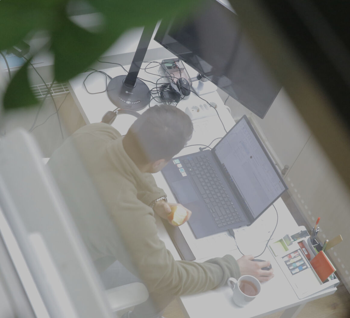 Person arbeitet an einem Laptop am Schreibtisch im Büro, aufgenommen aus erhöhter Perspektive