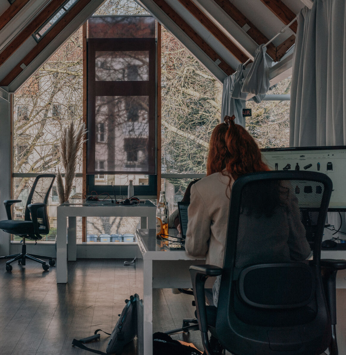 Mehrere Personen arbeiten konzentriert an ihren Schreibtischen in einem hellen, offenen Büro mit weißen Dachbalken und moderner Einrichtung