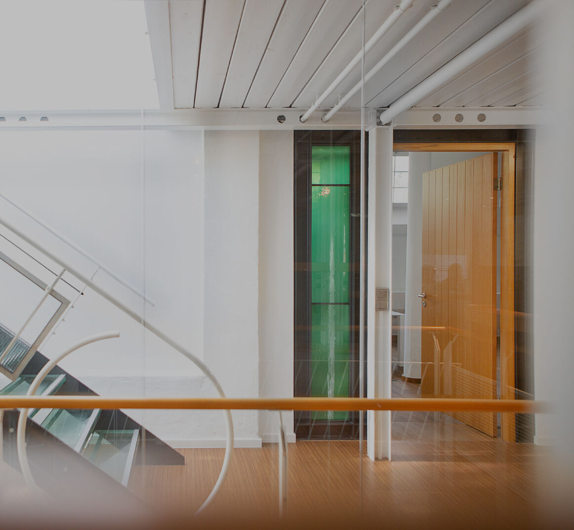Person arbeitet an einem Schreibtisch im Büro, seitlich durch eine Glaswand fotografiert